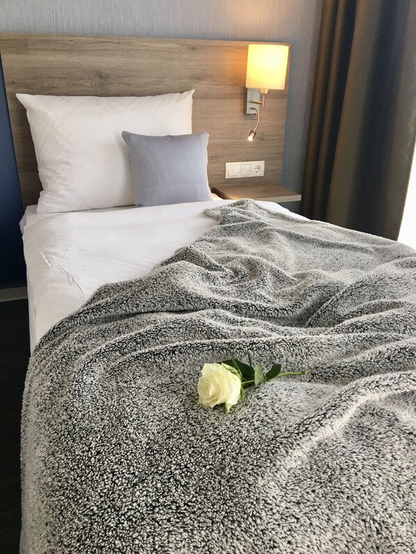 A neatly made bed with a fluffy blanket and a single white rose. - StadtHotel Arte (Remagen)