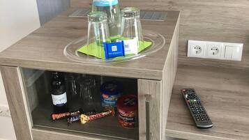 A wooden minibar with a bottle of Gerolsteiner, two glasses, a green napkin, and a remote control.