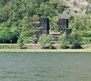 A historic stone building with multiple towers, surrounded by lush greenery and a body of water. - StadtHotel Arte (Remagen)