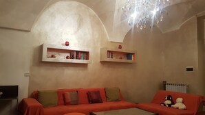 A living room with a sofa, two wall-mounted shelves with books, a radiator, and a chandelier. - Bed & Breakfast Alassio (Alassio)