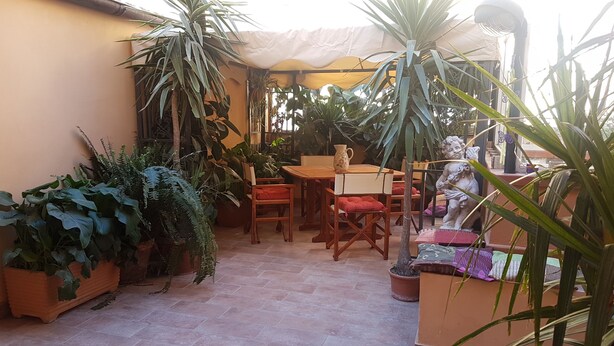 A patio area with a wooden table and chairs, surrounded by potted plants and a statue. - Bed & Breakfast Alassio (Alassio)