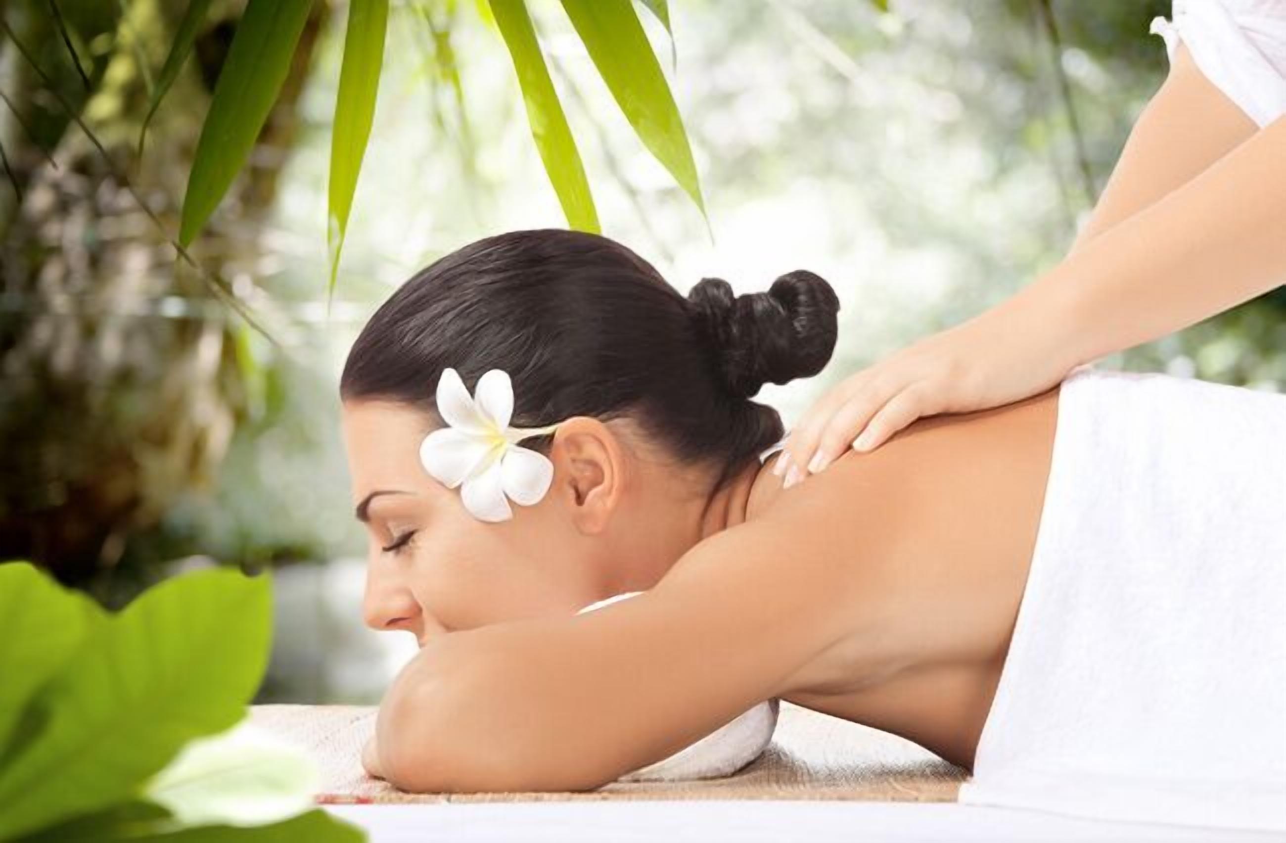 En person modtager en massage på ryggen i et spa-miljø med grøn vegetation i baggrunden.