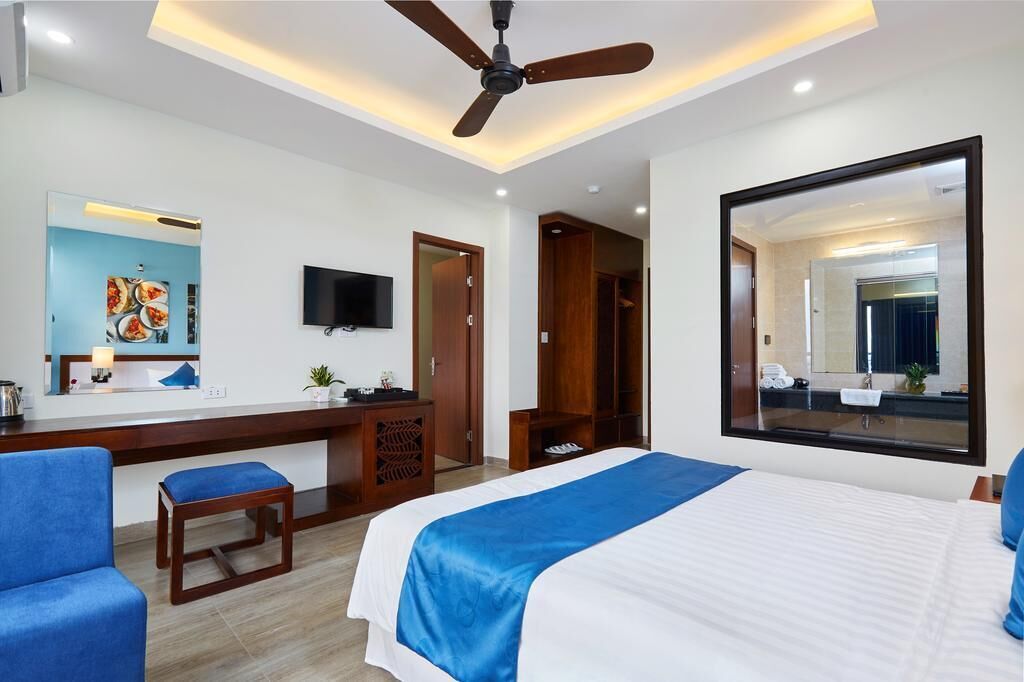A hotel room with a bed, a desk, a chair, a television, and a large mirror.