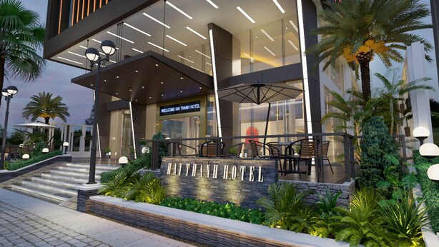 Une entrée d’hôtel moderne, agrémentée d’une enseigne accueillante, d’un espace extérieur aménagé pour s’asseoir et d’une végétation luxuriante.
