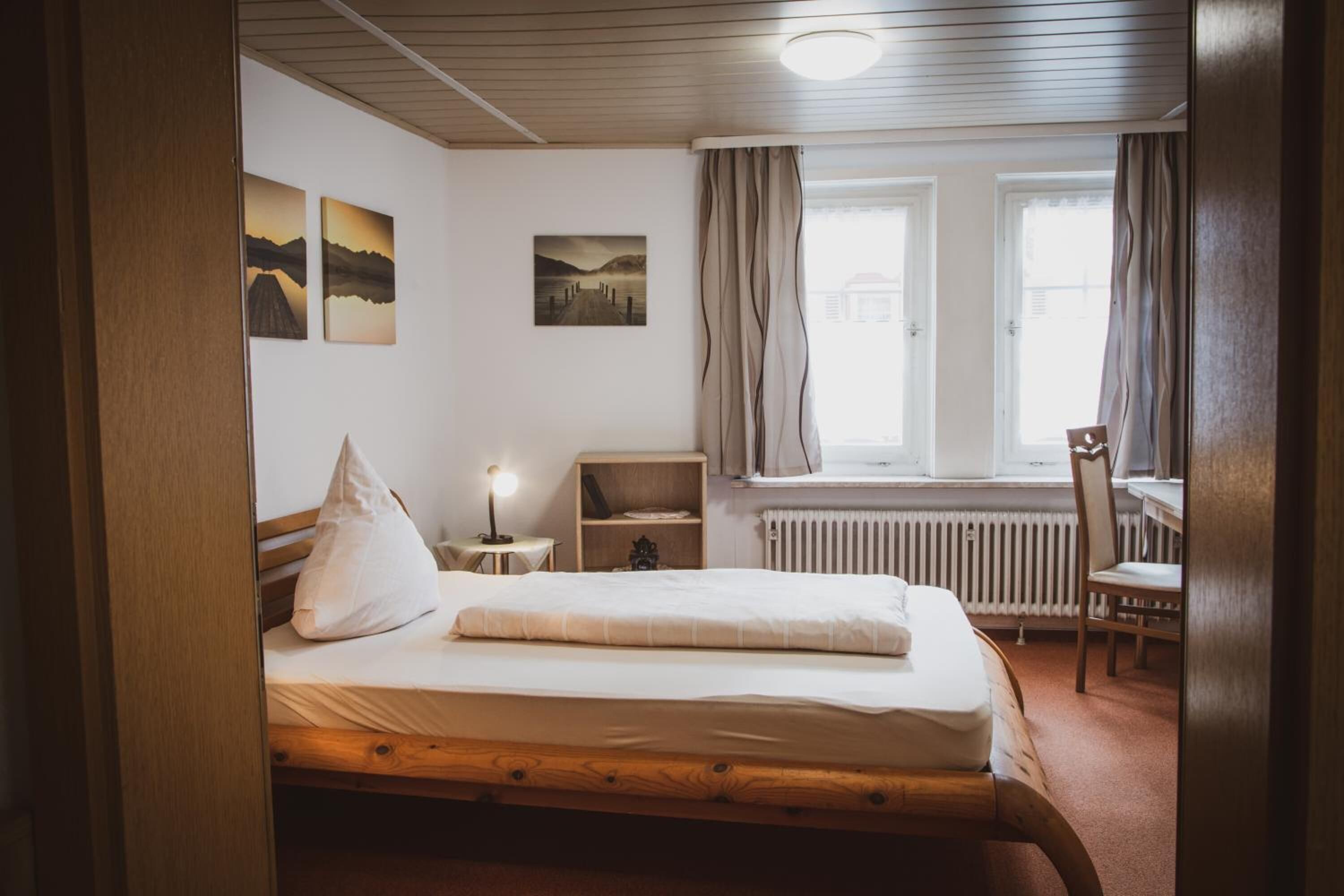 Ein Schlafzimmer mit einem hölzernen Bett, einem Nachttisch, einem Sessel, einem Heizkörper und einem Fenster mit Vorhängen.