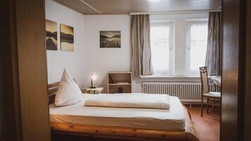 Un dormitorio con cama de madera, mesita de noche, una silla, un radiador y una ventana con cortinas.