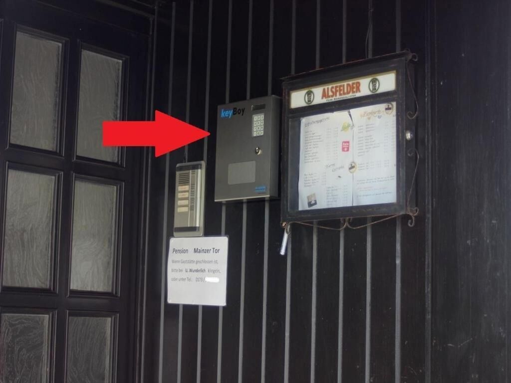 A door with a keypad lock, a sign for 'Pension Mainerz Tor', and a bulletin board with a notice titled 'ALSFELDER'.