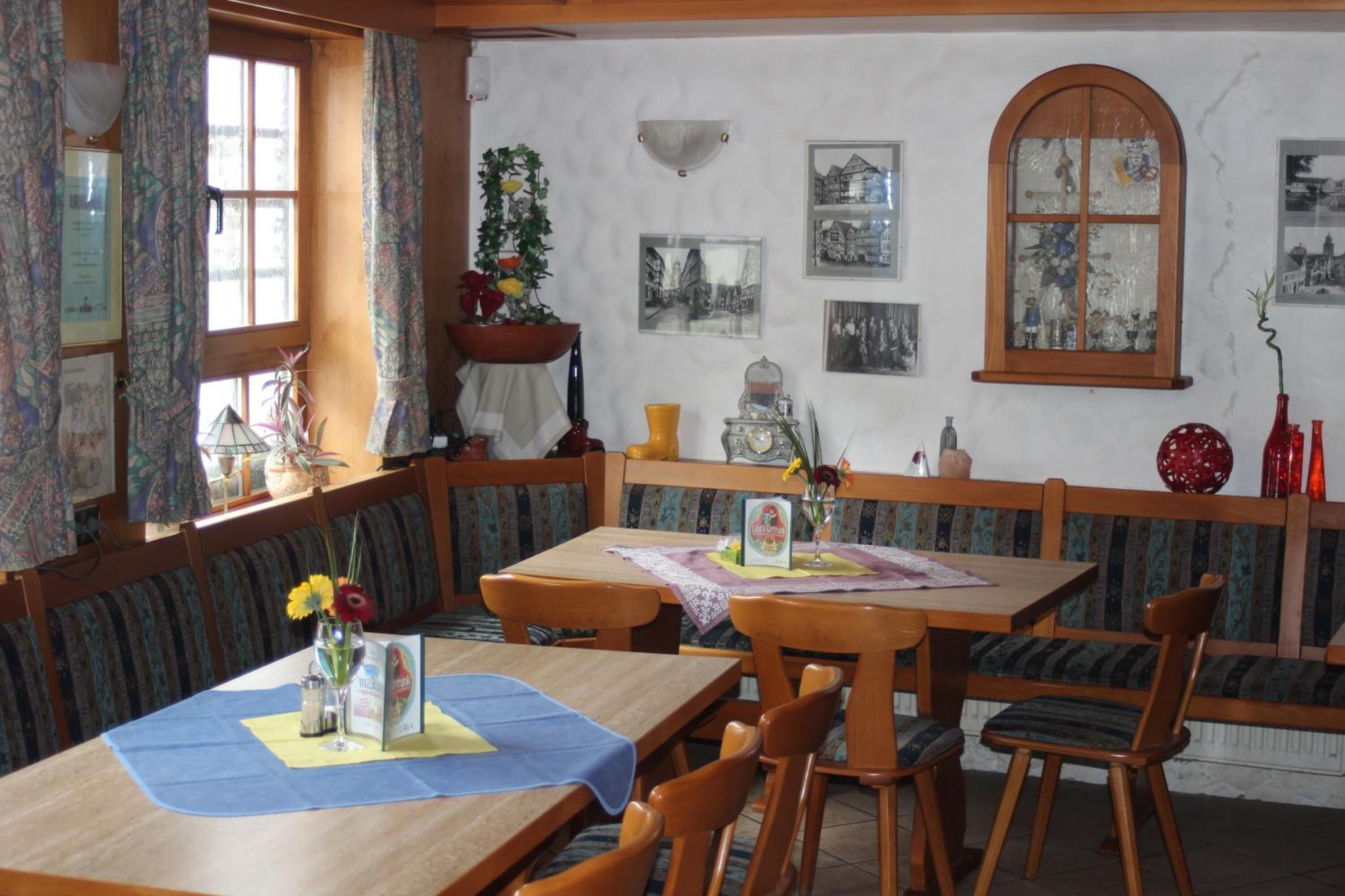 A dining area with wooden tables and benches, a large window with curtains, and wall-mounted pictures.