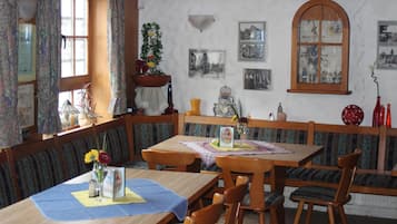 A dining area with wooden tables and benches, a large window with curtains, and wall-mounted pictures.