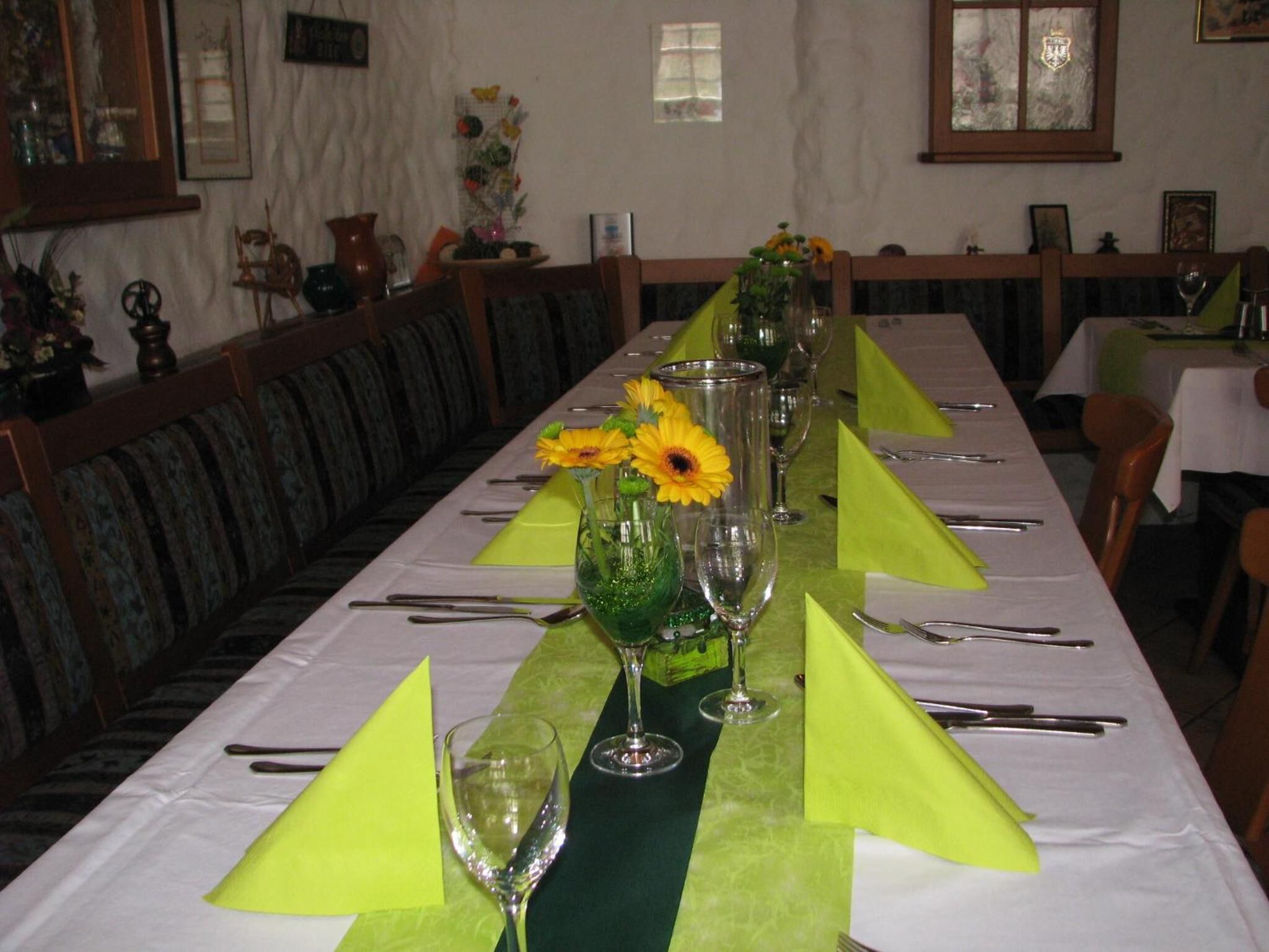 A long dining table set with green napkins, wine glasses, and a centerpiece with yellow flowers.