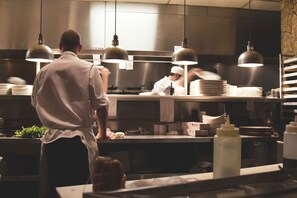 Una cocina profesional con chefs trabajando, electrodomésticos de acero inoxidable e iluminación colgante.