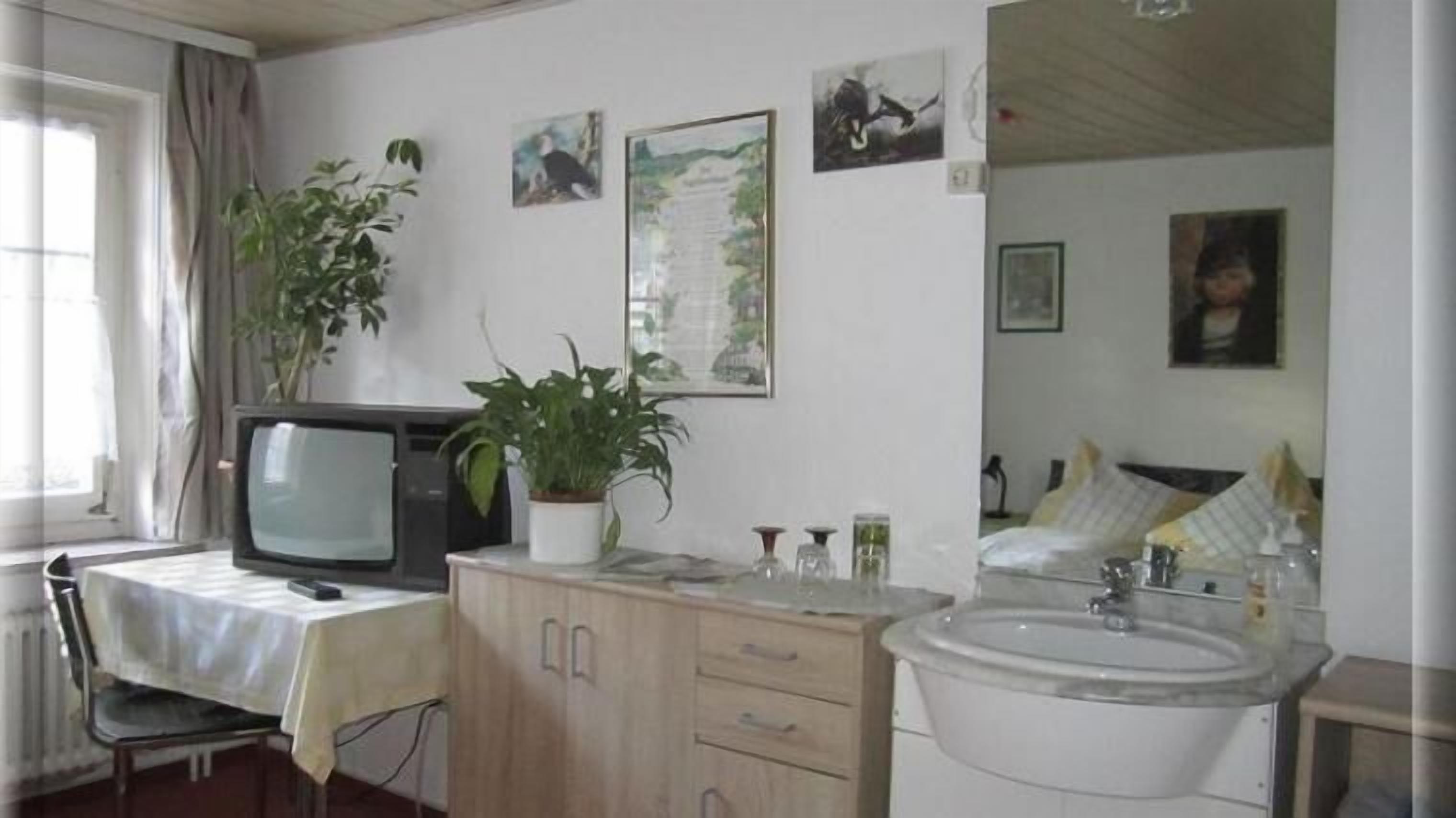 Una habitación pequeña y acogedora con televisión, lavamanos, armario y ventana con cortinas.