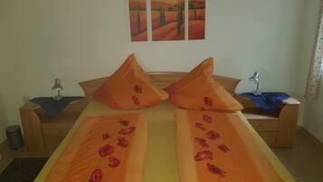 Una cama doble con ropa de cama naranja y diseños de amapolas, una mesita de noche con una lámpara y una pared decorada con tres cuadros.