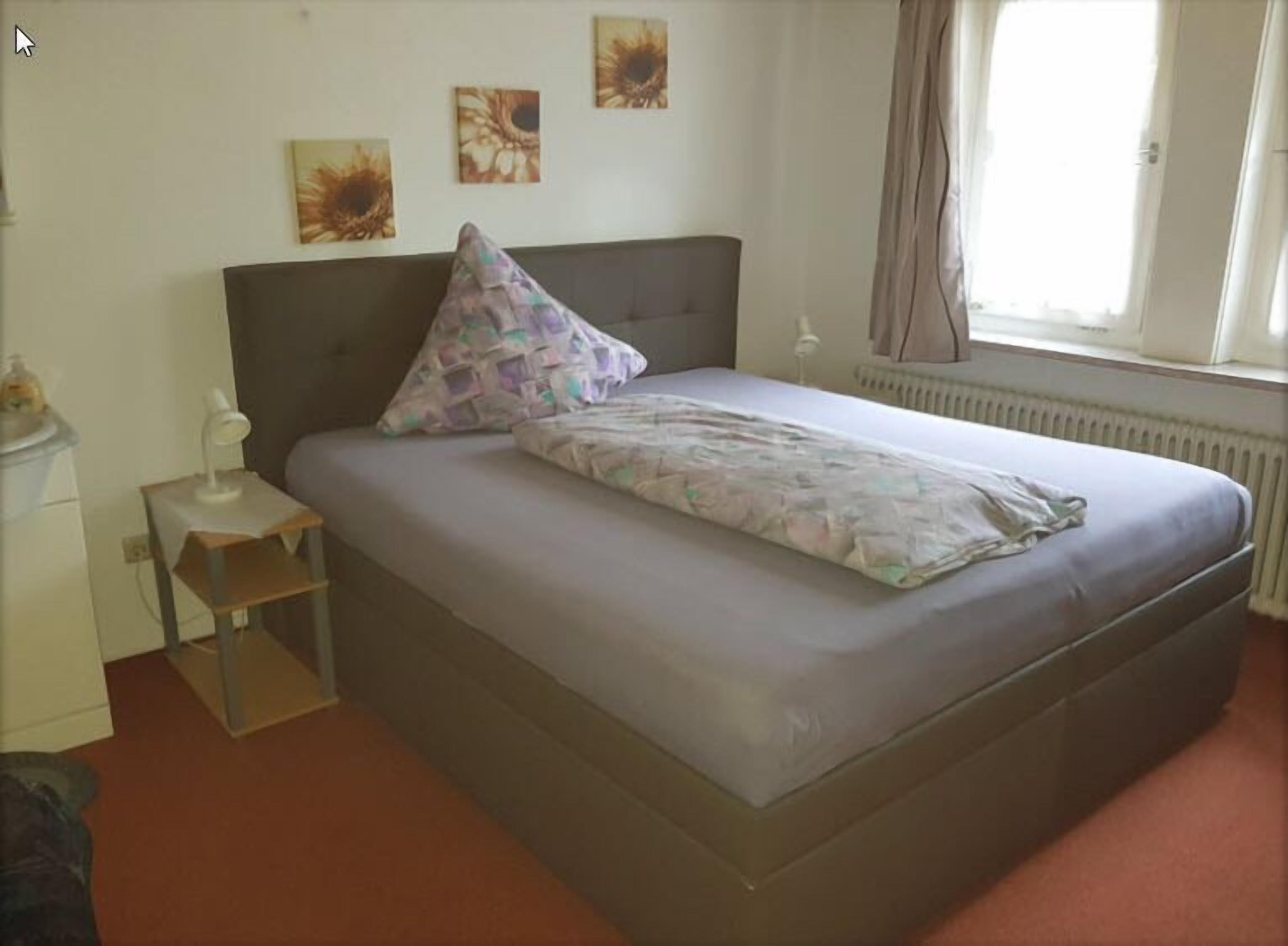 Een slaapkamer met een bed, nachtkastje, radiator en raam met gordijnen.
