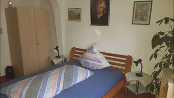A bedroom with a bed, wooden wardrobe, bedside table, lamp, and a potted plant.