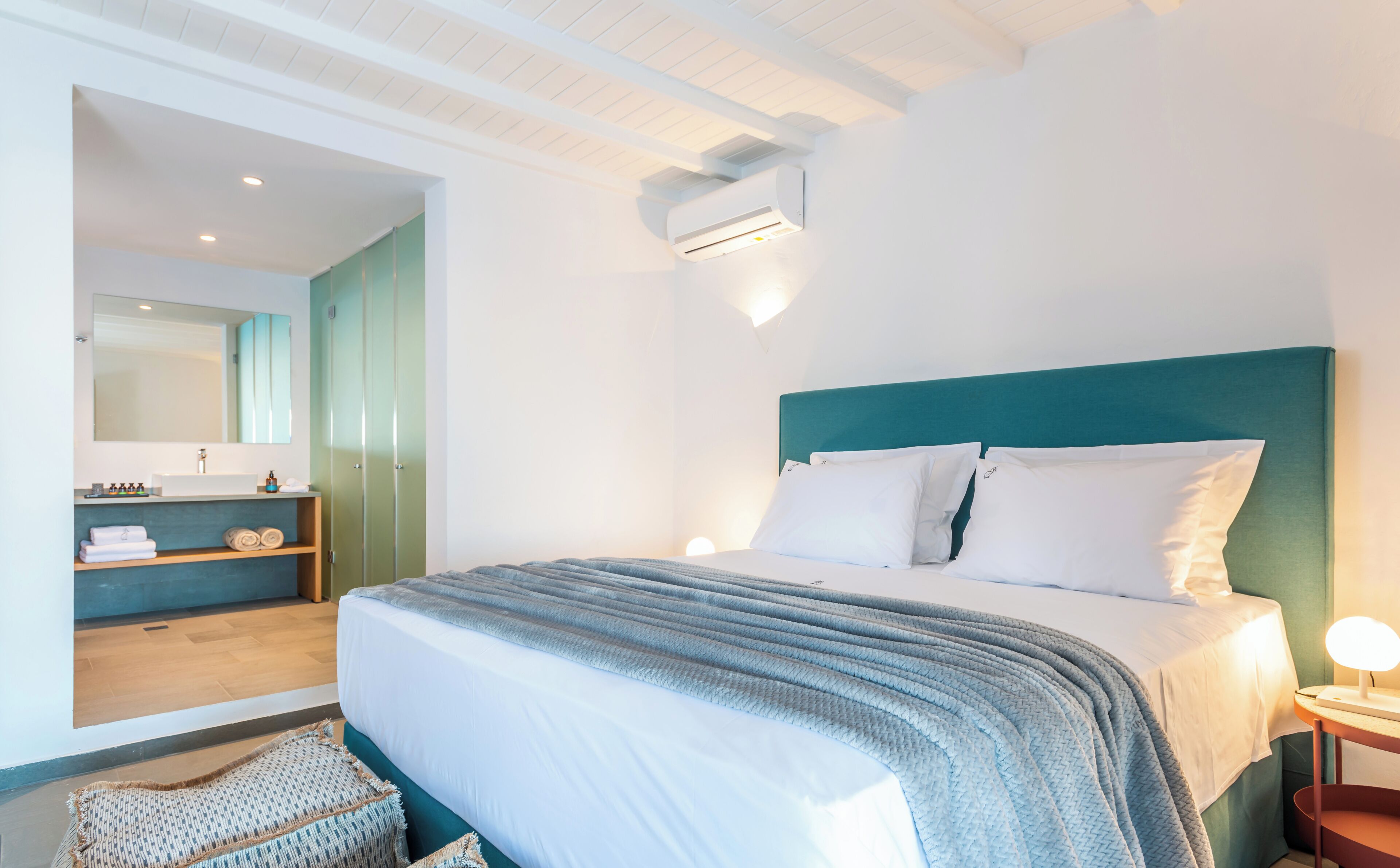 Quarto de hotel com cama, mesa de cabeceira, espelho, guarda-roupa e ar condicionado.