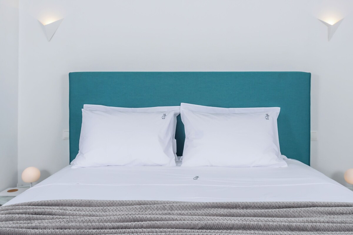 A neatly made bed with white bedding and a teal headboard.