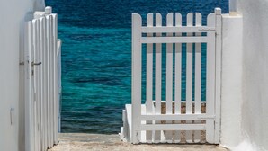 Una verja blanca que da a una zona costera con aguas azul turquesa y montañas al fondo.