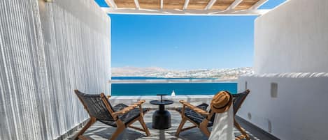 Una terraza con vista al mar, dos sillas de mimbre, una mesita redonda y un vestido blanco en el suelo.