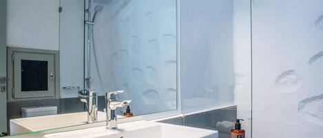 A modern bathroom with a large mirror, a white sink, and a glass shower enclosure.