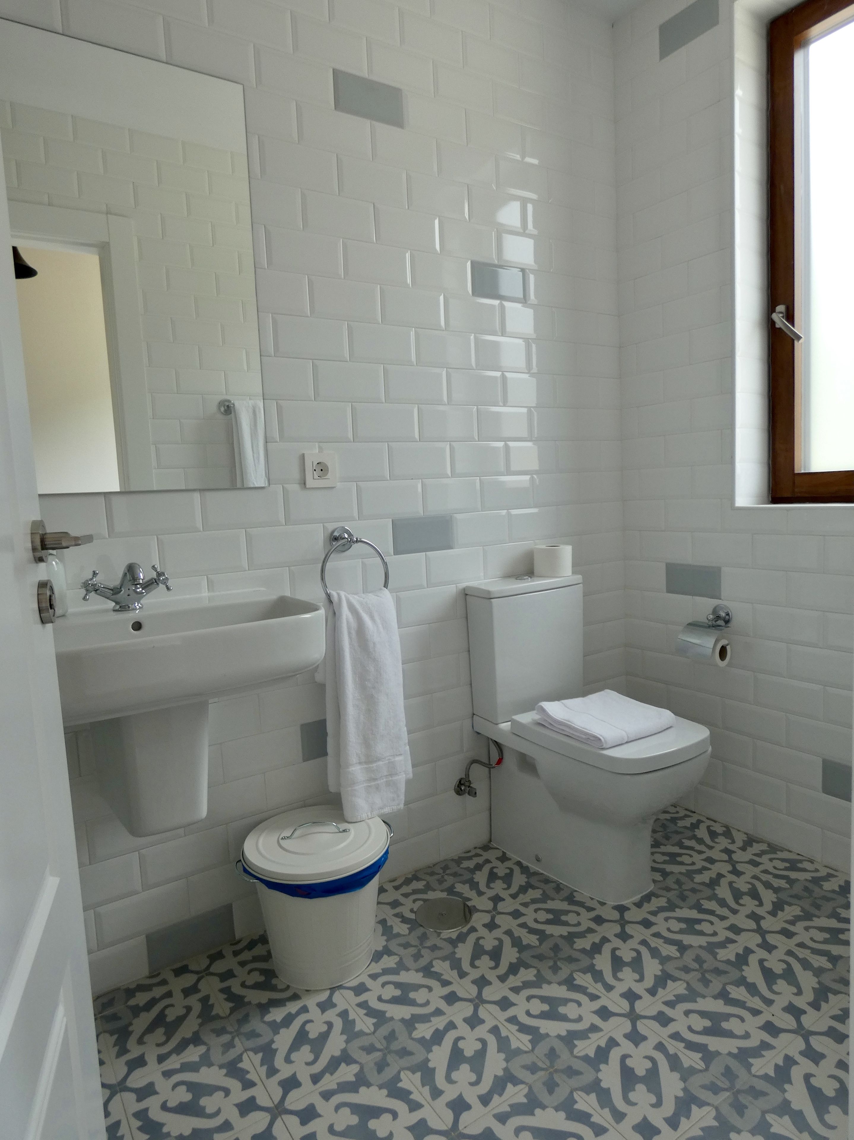 A bathroom with white subway tiles, a sink, a toilet, and a patterned floor.
