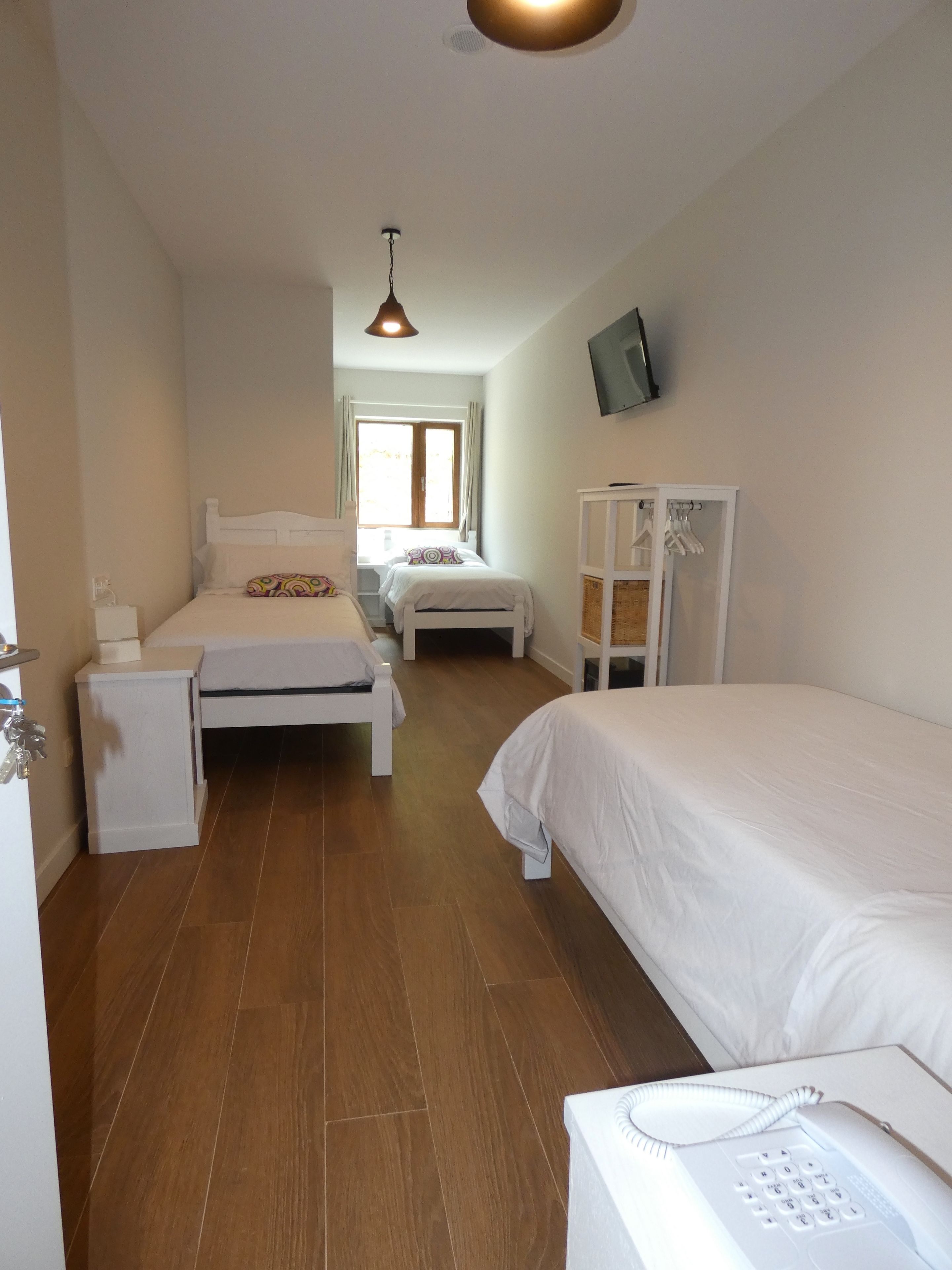 Une chambre avec deux lits, une table de chevet, une armoire, un téléviseur fixé au mur et un téléphone.