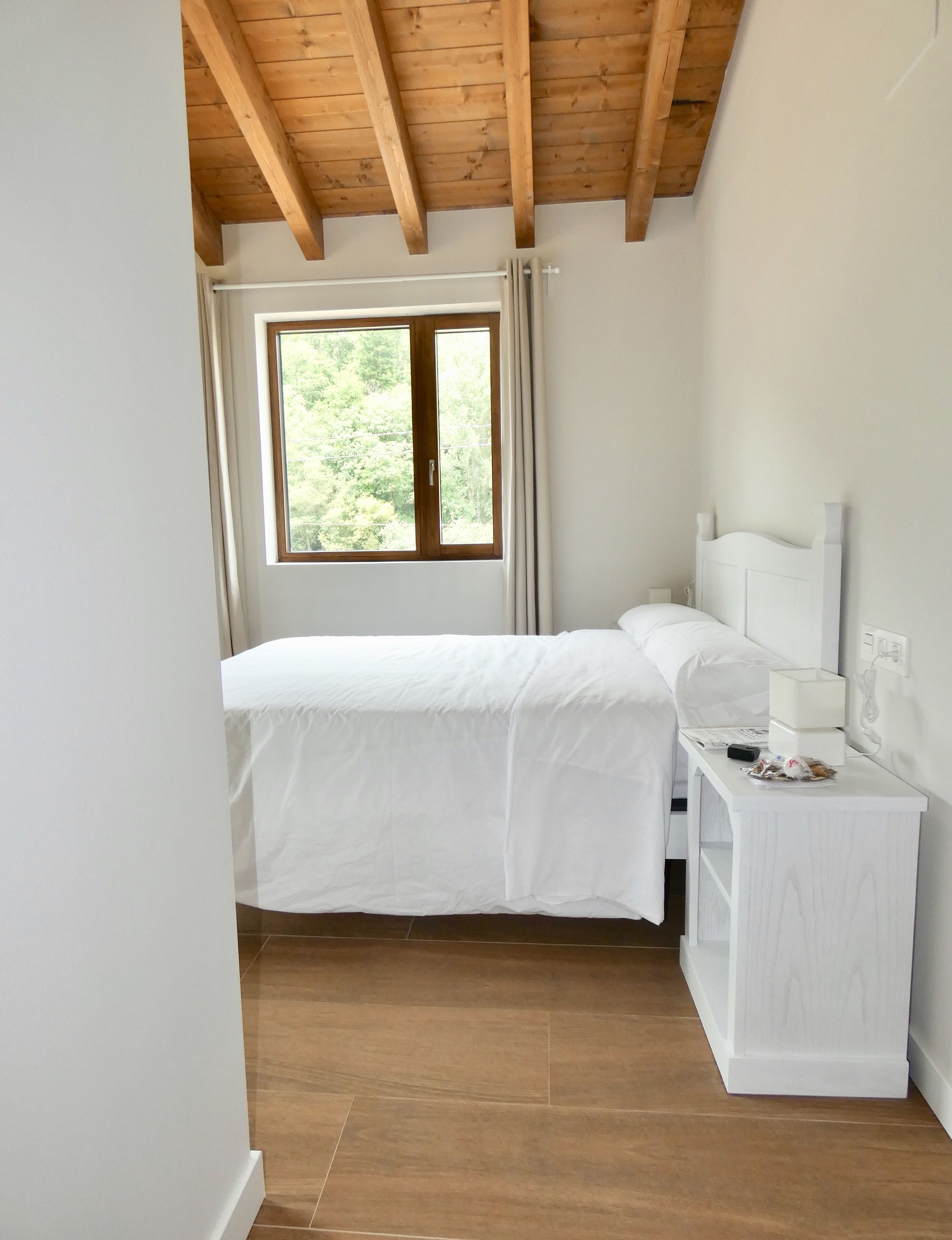 Une chambre à coucher avec un lit, une table de chevet, une fenêtre avec des rideaux et un plafond en bois.