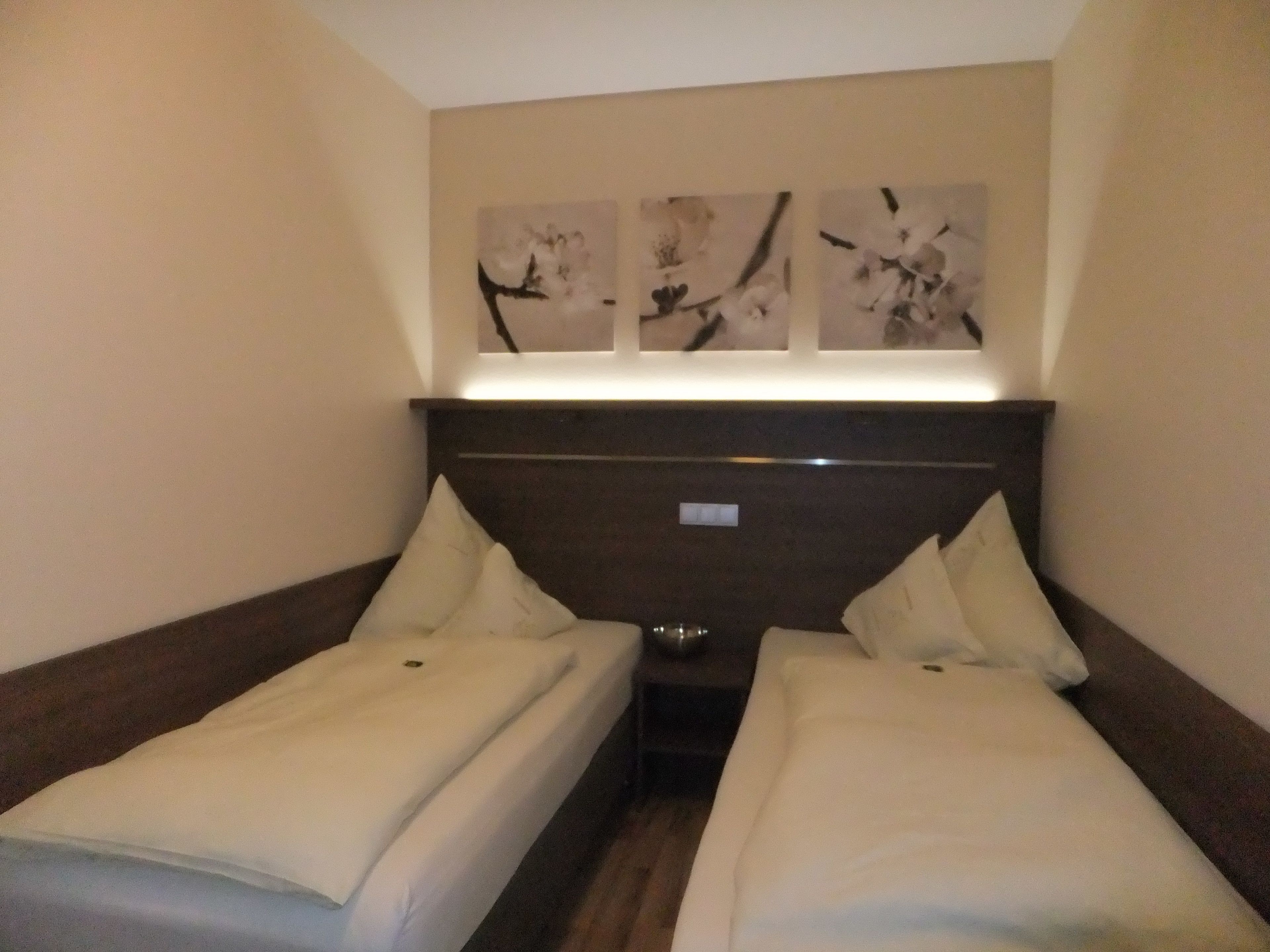 A hotel room with two single beds, a dark headboard, and three wall-mounted artworks.