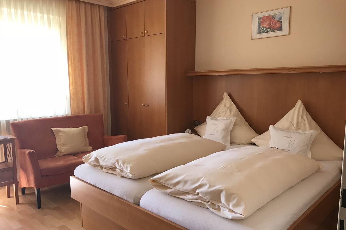 Ett hotellrum med en dubbelsäng, en garderob i trä, en liten fåtölj och ett bord.