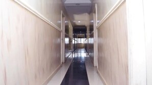 Un pasillo largo y estrecho con paredes de colores claros y suelo negro, que conduce a una escalera.