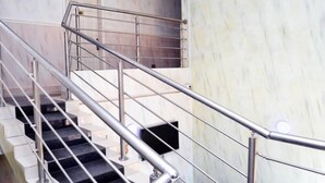 Una escalera con barandillas metálicas y peldaños negros, que conduce a un rellano con una puerta.