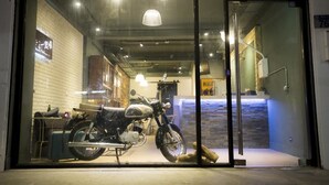 A motorcycle displayed in a glass window of a building with a brick wall and a staircase visible in the background. - 176 Together Hostel (Hualien City)