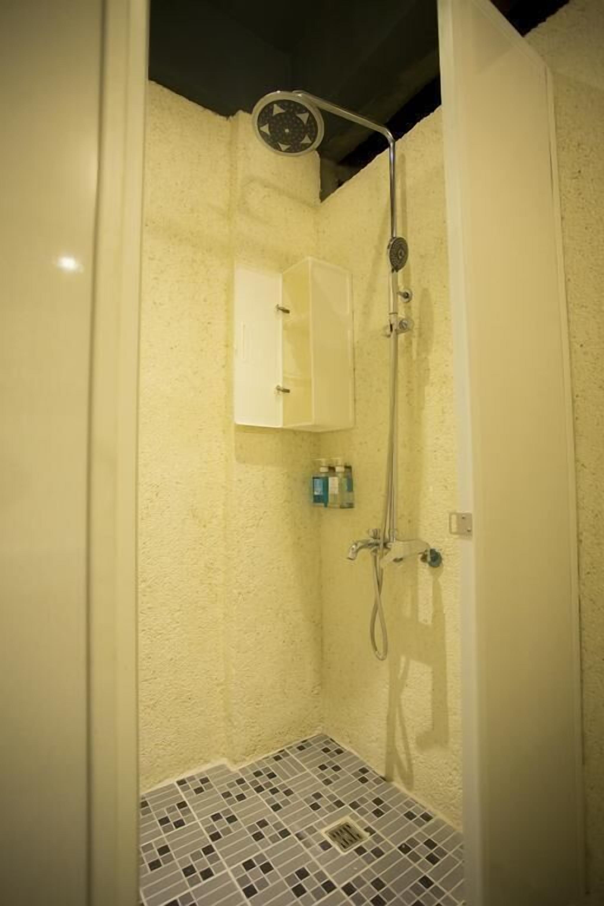 A small, enclosed shower area with a tiled floor and a white cabinet above the shower.