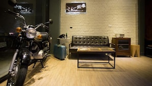 A motorcycle parked next to a leather sofa and a small wooden table in a room with a brick wall and a mirror. - 176 Together Hostel (Hualien City)