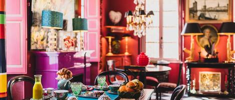 A dining area with a checkered floor, a table set with various dishes and drinks, and a vibrant red and pink color scheme.