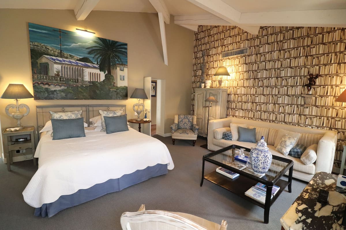 A hotel room with a large bed, a sofa, a coffee table, and a bookshelf.
