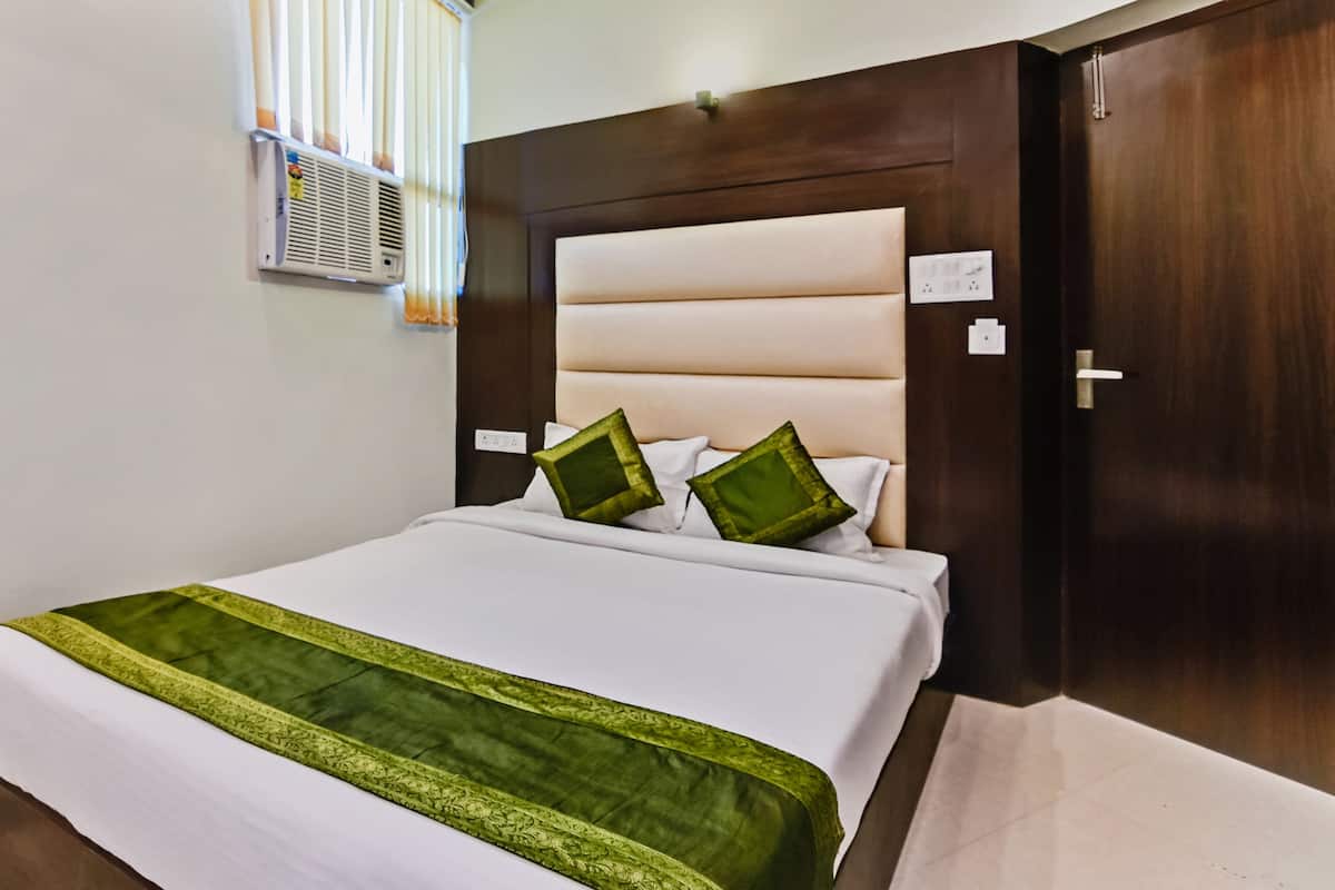 A hotel room with a bed, a wooden headboard, and a window with blinds.