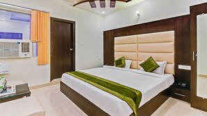 Habitació d'hotel moderna amb un llit gran, un panell de fusta al capçal, una taula de nit amb un telèfon i una finestra amb cortines.