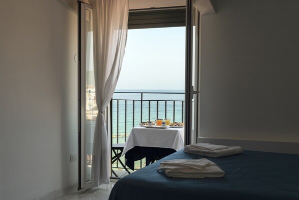 A balcony with a table set for breakfast, a bed with towels, and a view of the sea. - Residenza d'Epoca Olimpia (Castellabate)