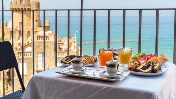 A breakfast table with croissants, fruit, and juice, overlooking a coastal view with a tower in the background. - Residenza d'Epoca Olimpia (Castellabate)