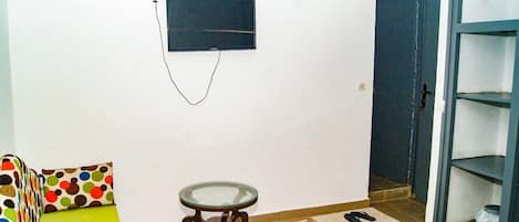 A small room with a sofa, a small table, a TV mounted on the wall, and a door leading to another room.