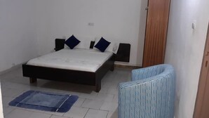 A bedroom with a bed, bedside tables, a chair, and a small rug. - Hotel Restaurant du 3ème Pont (Abidjan)