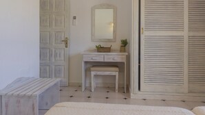 A bedroom with a white dresser, a mirror, a bench, and a closet with louvered doors. - Aptos Barbarroja - Formentera Break (Formentera)