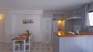 A compact kitchen with a wooden table and chairs, a small island with a sink, and a tiled backsplash. - Aptos Barbarroja - Formentera Break (Formentera)