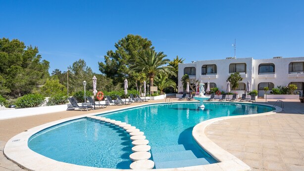 A swimming pool with lounge chairs and umbrellas, surrounded by greenery and a building with multiple windows. - Aptos Barbarroja - Formentera Break (Formentera)