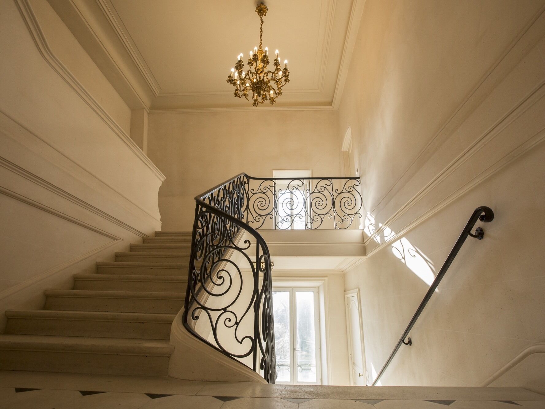 Een statige trap met versierde, zwarte balustrades en een kroonluchter.