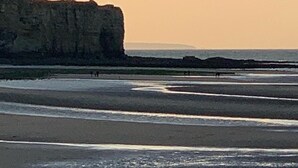 Een kustlandschap met een grote rotsformatie en een strand waar mensen lopen.