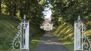 Een pad dat leidt naar een huis met versierde witte poorten, omgeven door weelderige begroeiing.