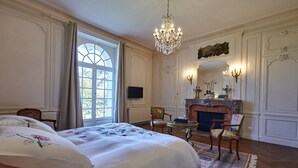 Een ruime slaapkamer met een groot bed, een open haard en een kroonluchter.