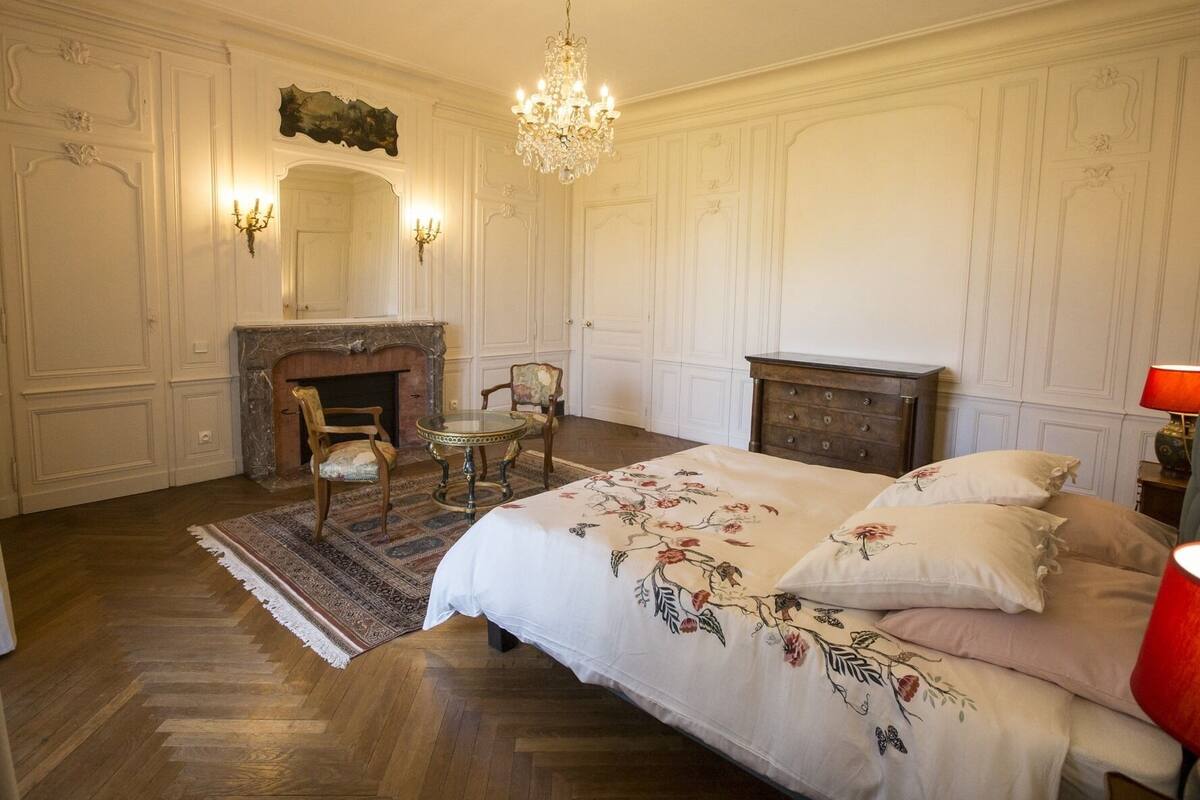 Ein klassisches Schlafzimmer mit Kamin, einer Chandelüster und einem Bett mit floralem Bettzeug.